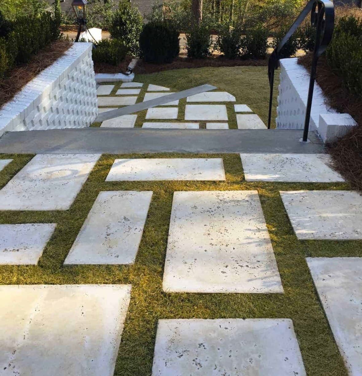 Large pale stone pavers set in grass, stepping up between white brick walls toward a front entry