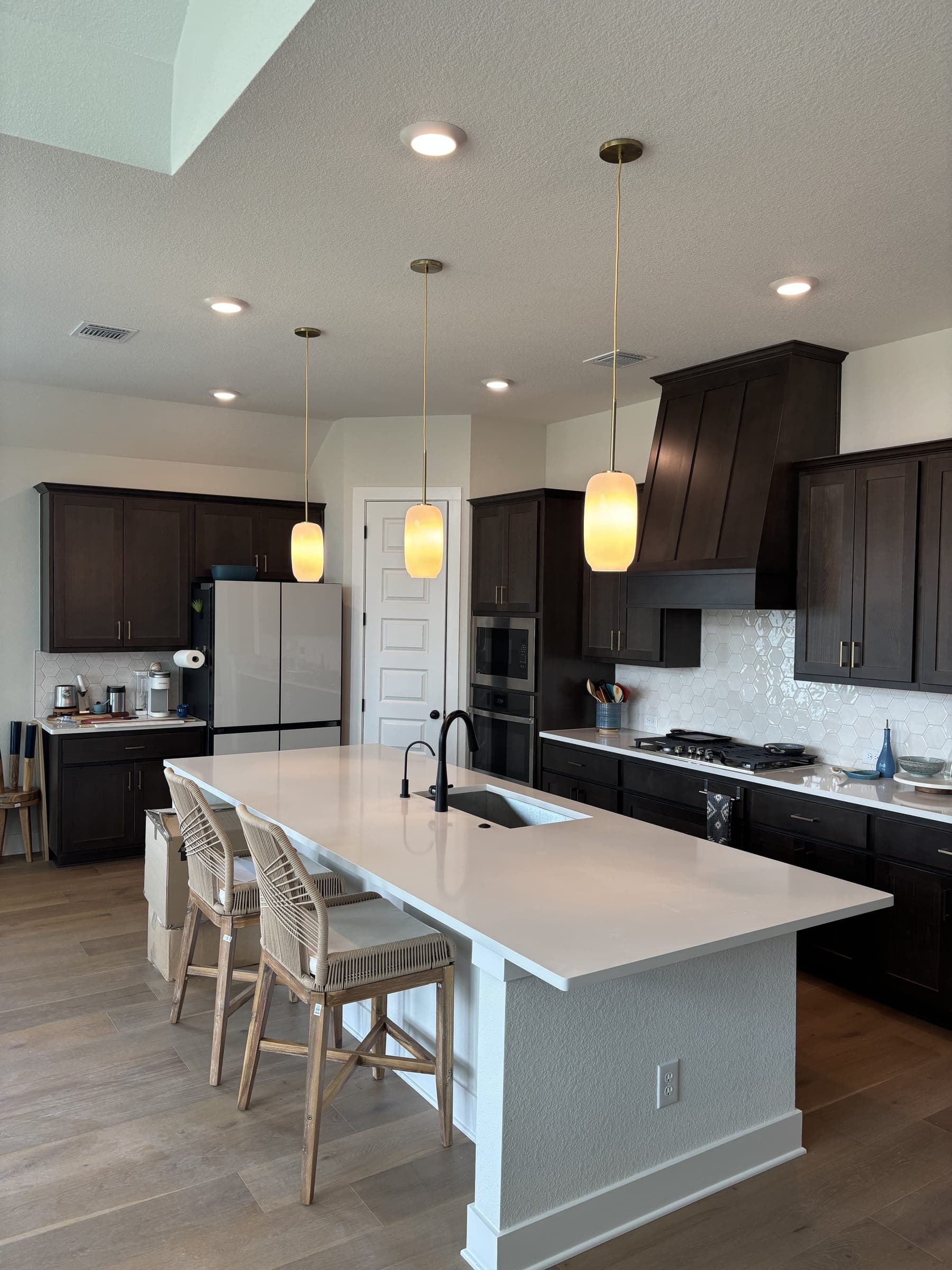 Finished kitchen with dark cabinetry, quartz island and amber glass pendants