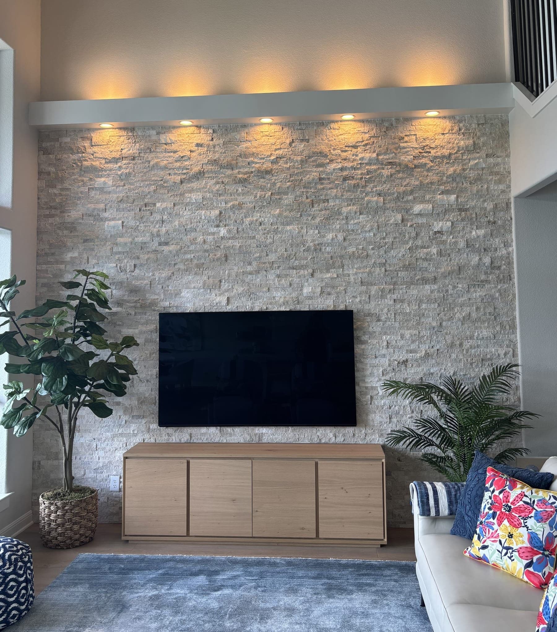 Stacked stone feature wall lit from above, with a mounted television and a pale oak credenza