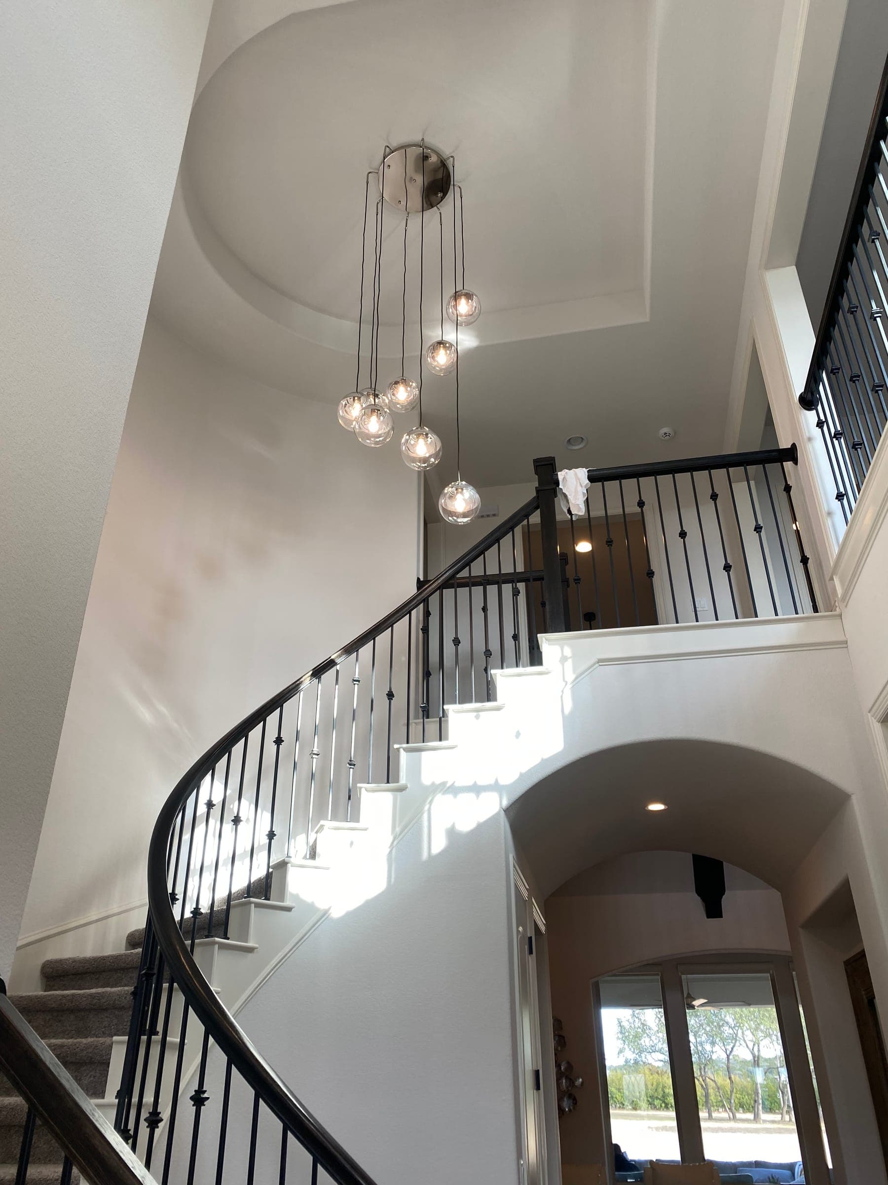 Cascading glass pendants falling through a curved staircase in a double-height entry