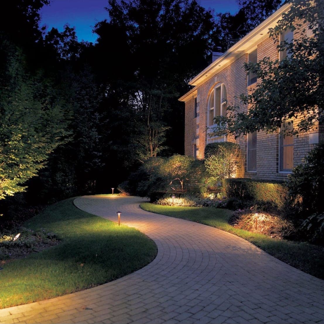 Brick home at dusk with landscape uplighting along a curved paver path
